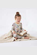 Child in floral pajamas reading a book on a white background