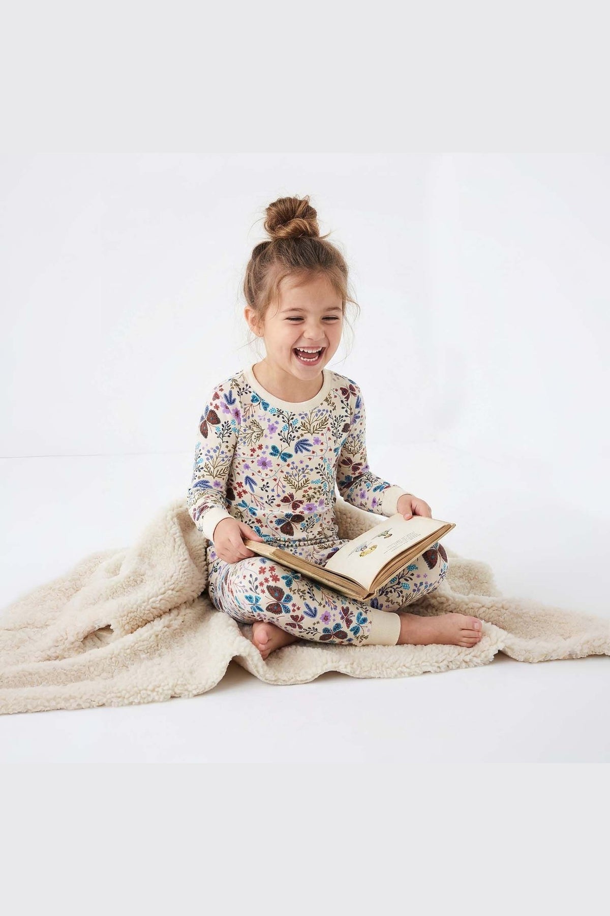 Child in floral pajamas reading a book on a white background