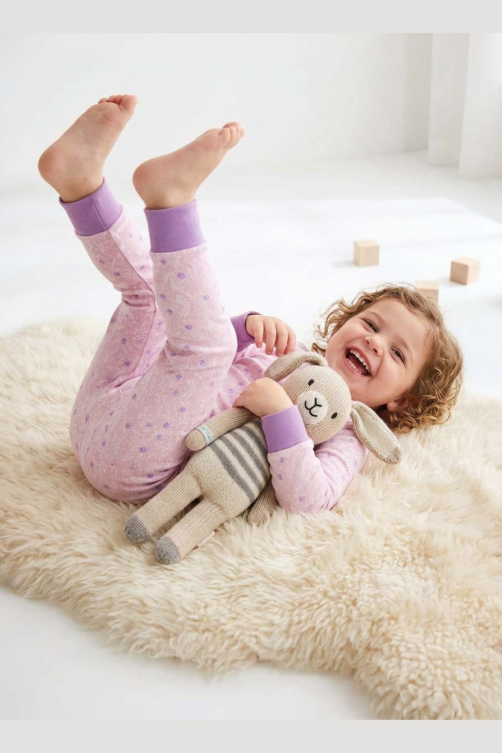 Child in pink pajamas with a plush toy on a fluffy rug