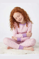 Child wearing pink pajamas with purple cuffs and trim sitting on a white surface.