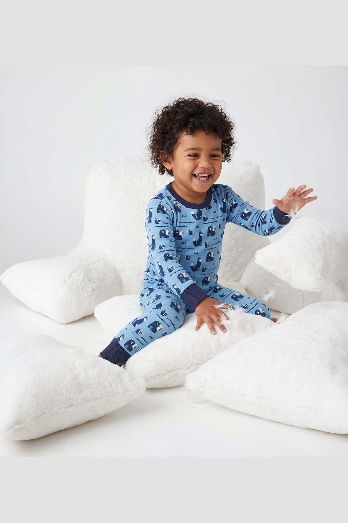 Child wearing blue pajamas with animal pattern sitting on white pillows. 
