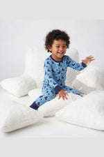 Child wearing blue pajamas with animal pattern sitting on white pillows. 
