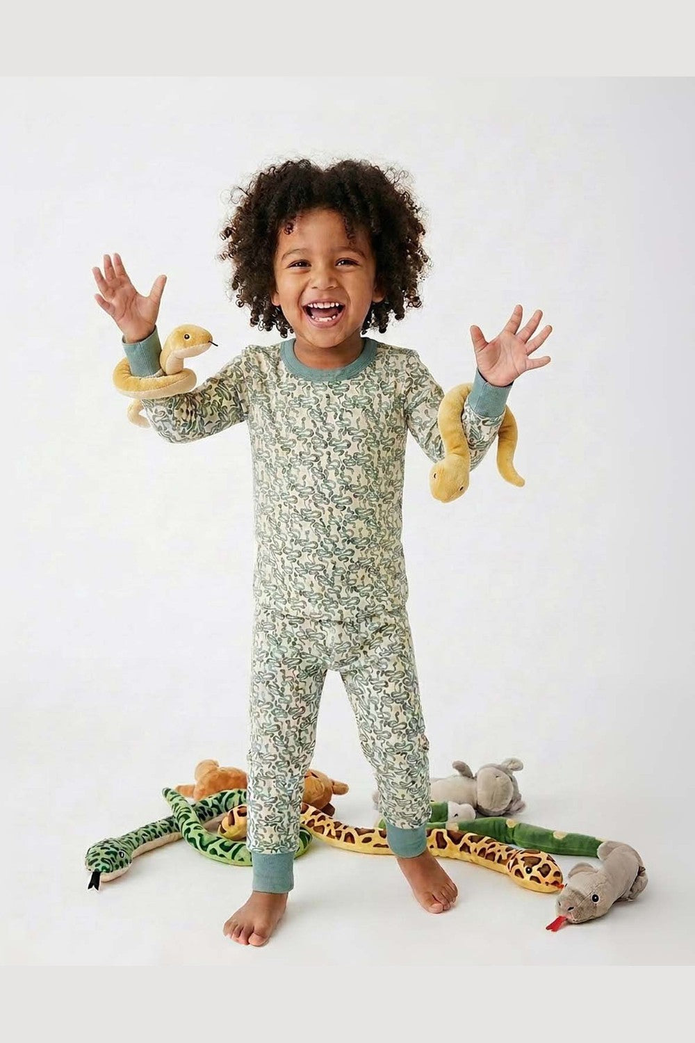 Child wearing a green snake pajamas with toys on a white background 
