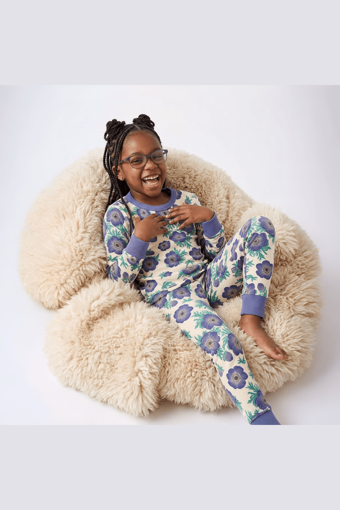 Child wearing a floral pajama set sitting on a fluffy chair.