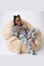 Child wearing a floral pajama set sitting on a fluffy chair.
