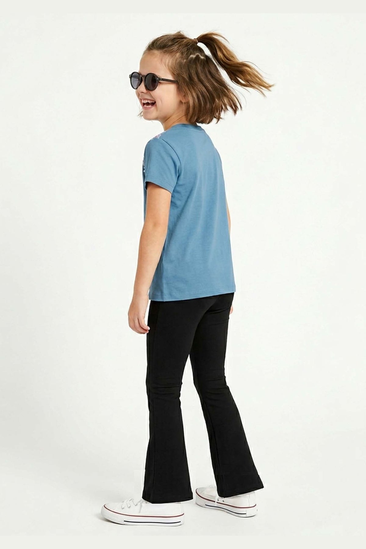 Child wearing a blue t-shirt and black flared yoga pants on a white background
