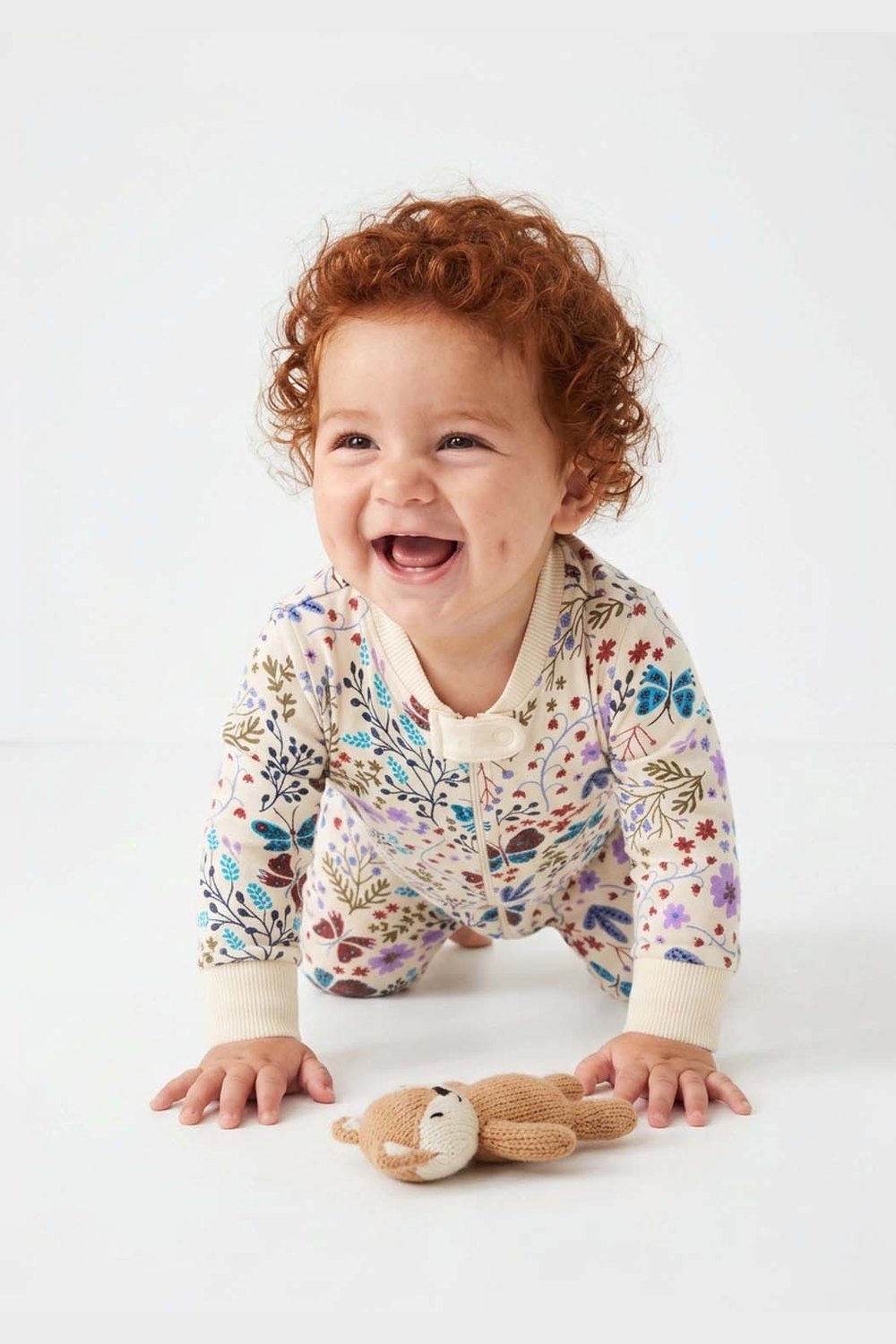 Baby in a floral onesie with a toy on a white background 