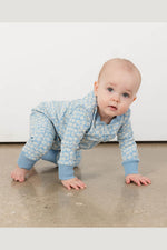 A baby crawling on a concrete floor wearing a light blue and white patterned one-piece jumpsuit. 