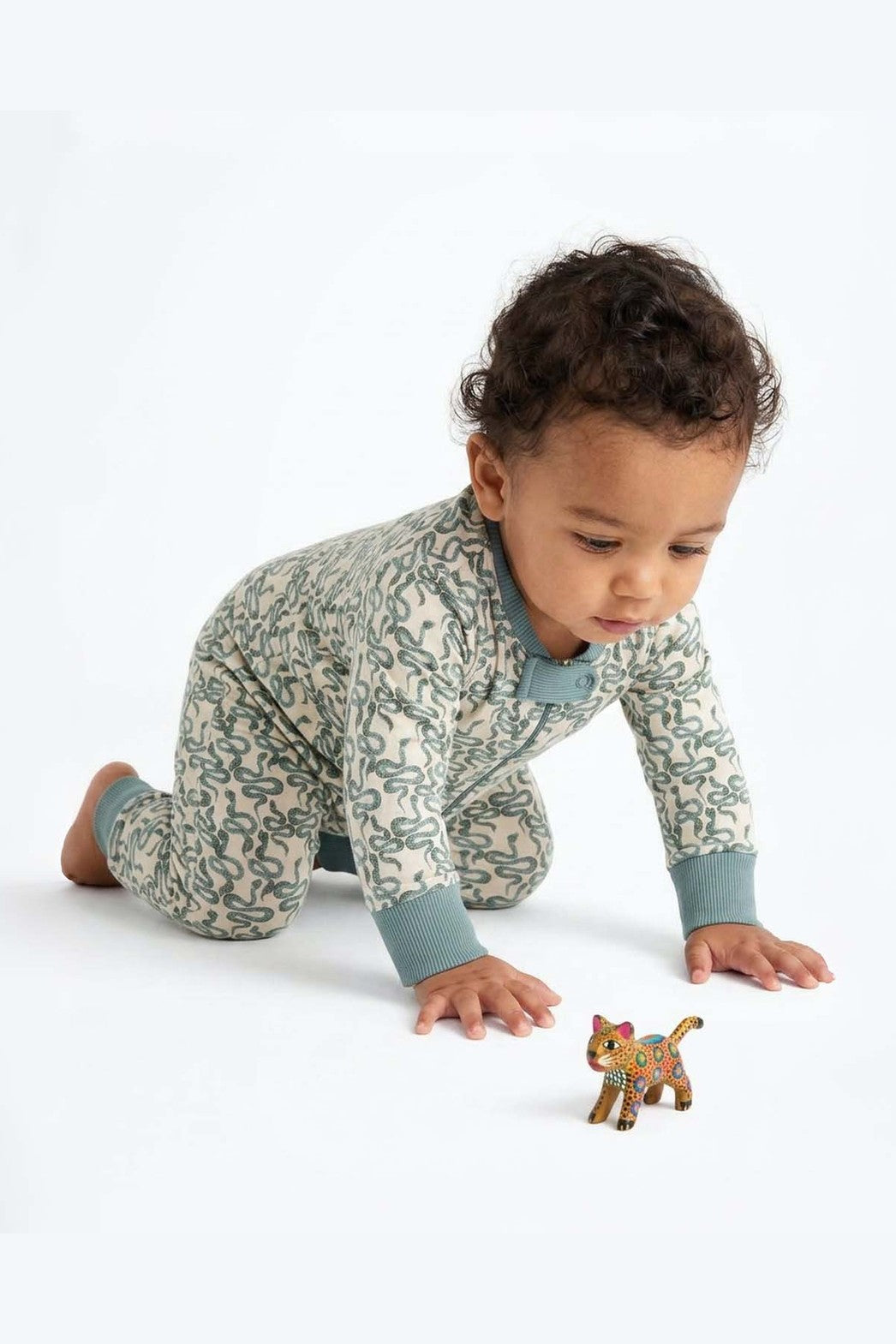 Baby crawling wearing pajamas with green snakes on a white background 