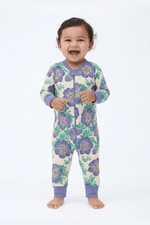 Baby wearing a floral patterned onesie with purple flowers on a white background 