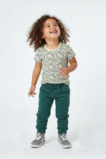 Child wearing a snake patterned shirt and green pants on a white background 