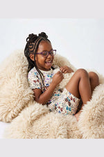 Young girl with braided hair wearing pajamas and glasses, sitting on a fluffy chair. 