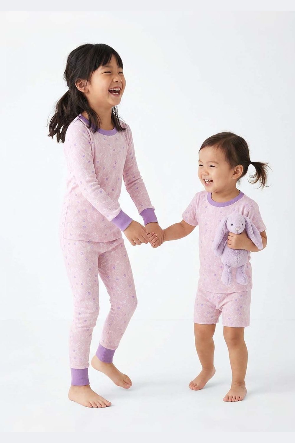 Two children wearing pink pajamas holding hands on a white background 