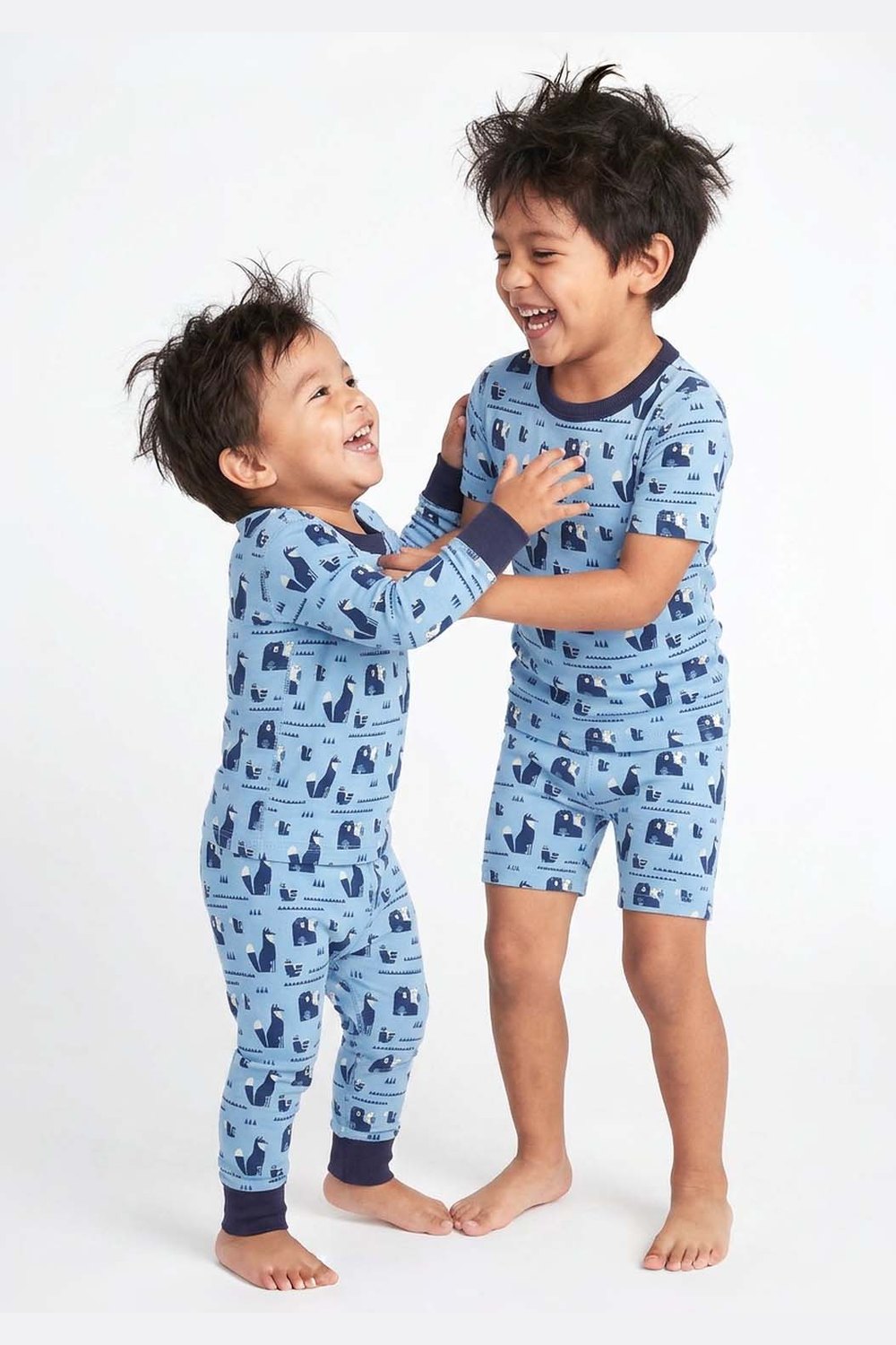 Two children wearing blue pajamas with a pattern, standing on a white background 