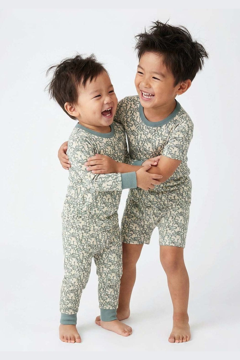 Two children wearing matching green snake pattern pajamas on a white background