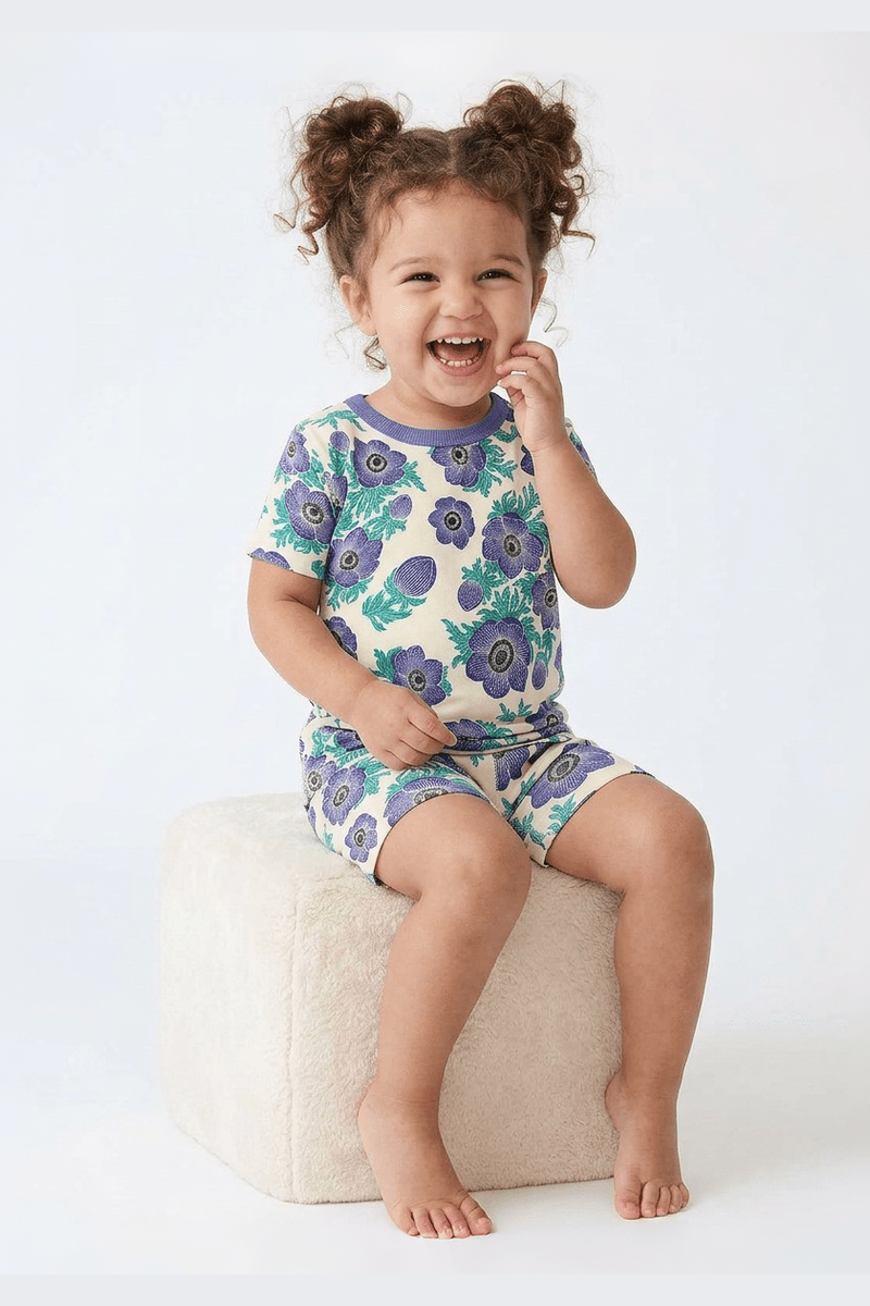 Child wearing a floral pajama set sitting on a white stool against a white background 