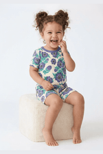 Child wearing a floral pajama set sitting on a white stool against a white background 