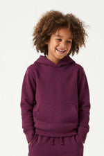 A smiling child with curly brown hair wearing a matching deep purple hoodie and sweatpants set, photographed against a clean white studio background. 