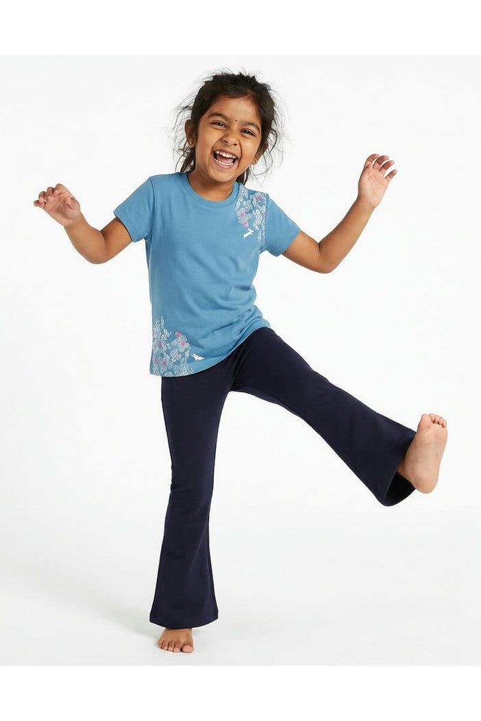 Young girl wearing a Mightly 100% organic cotton graphic tee with a pink and white print featuring flowers and bunnies and navy blue pants. 