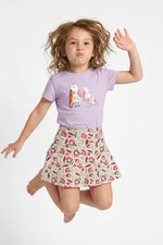 Young girl jumping. She is wearing a Mightly 100% organic cotton graphic tee with a colorful bird print and a floral skirt.  