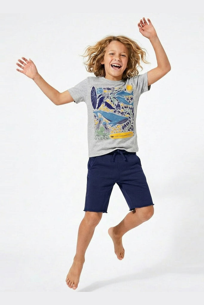 Child wearing a gray t-shirt with a colorful design and navy shorts, jumping on a white background 