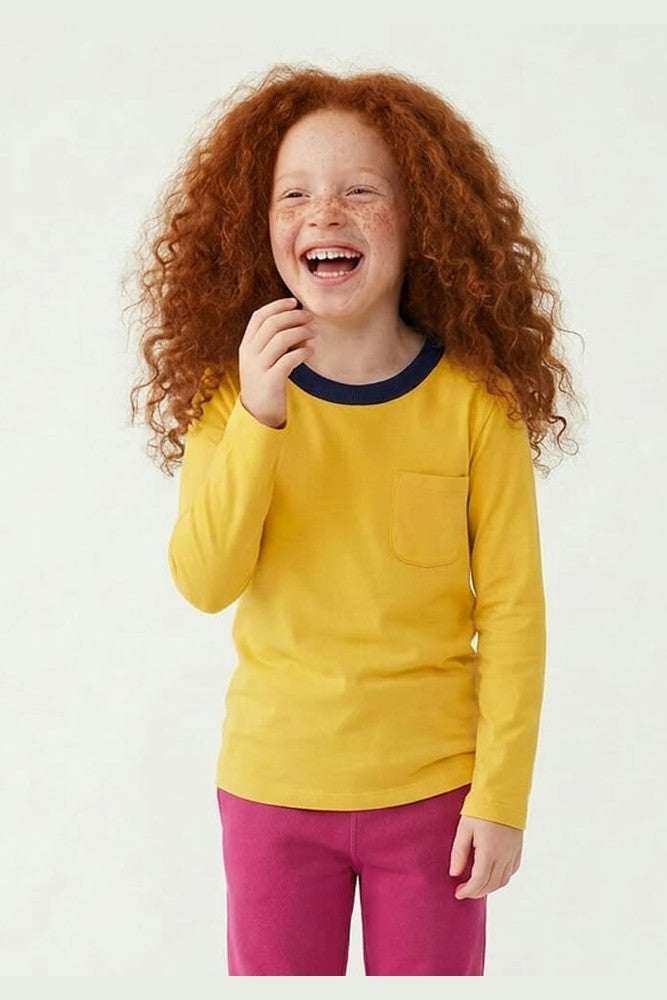 Child wearing a yellow long-sleeve shirt with a pocket and pink pants on a white background