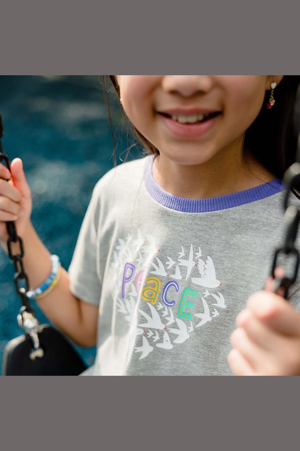 Child wearing a gray t-shirt with 'PEACE' printed on it, holding onto something with a blurred background.