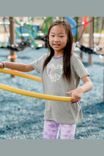 Young girl playing with a yellow hula hoop on a playground. Wearing a gray tee shirt with peace printed on it.
