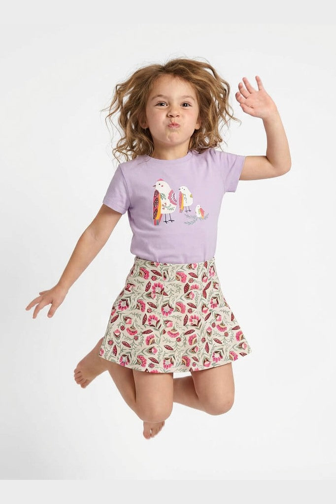 Child wearing a purple t-shirt with a colorful design and a floral skirt on a white background