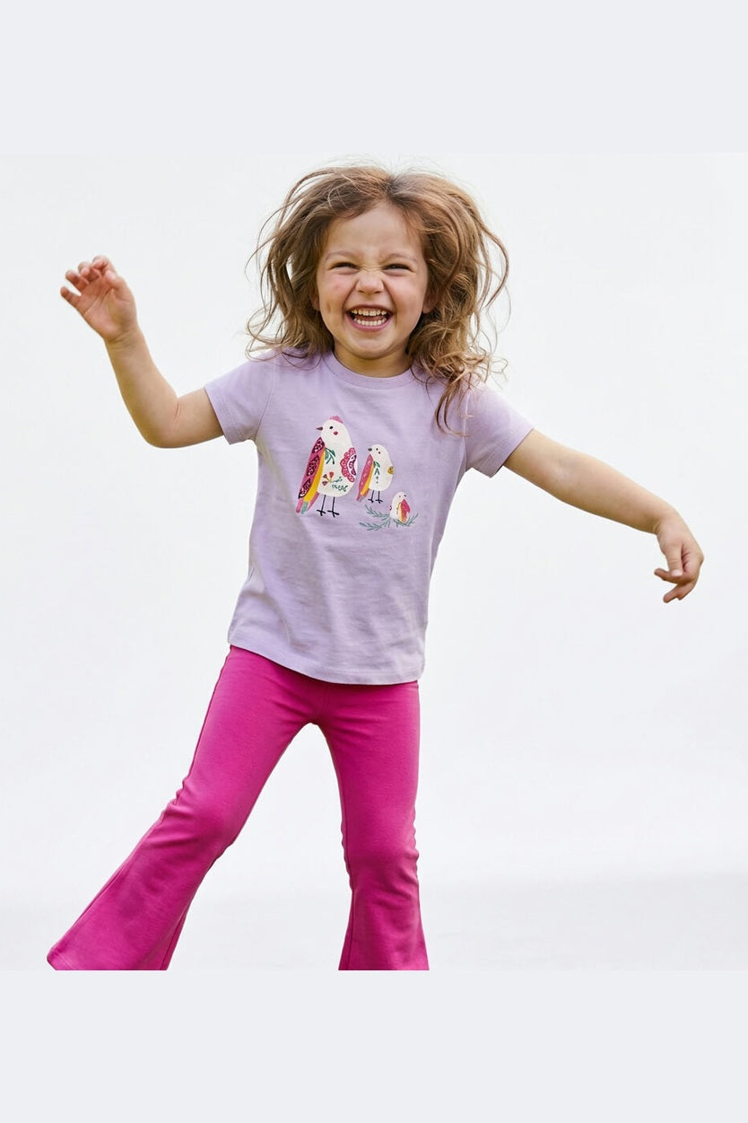 Child wearing a purple shirt with a colorful bird design and pink pants on a white background