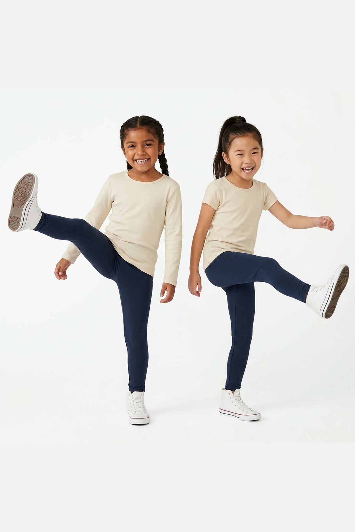 Two young girls wearing navy leggings and cream tops on a white background