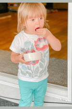A toddler wearing a white shirt with a floral print eating strawberries