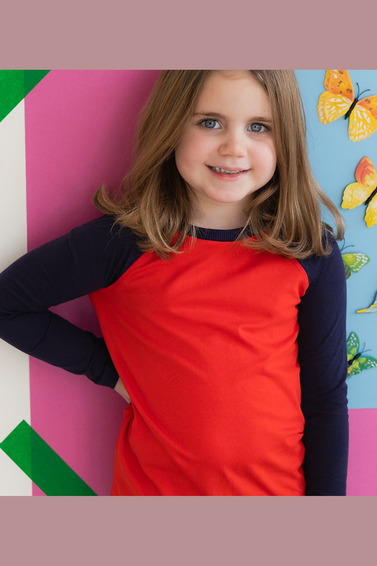Young girl wearing a navy and red long sleeve tee shirt against a colorful wall