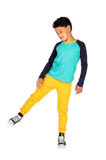 a boy in an active pose wearing a navy and teal long sleeve baseball tee and yellow sweatpants 