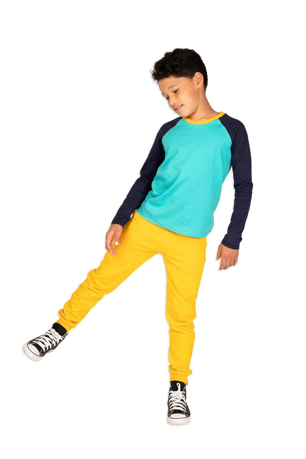 a boy in an active pose wearing a navy and teal long sleeve baseball tee and yellow sweatpants 
