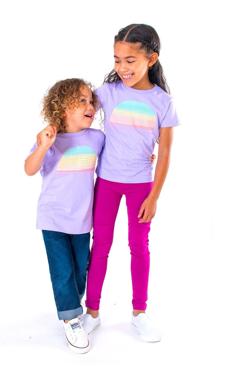 Two children wearing matching purple t-shirts with a rainbow design on a white background