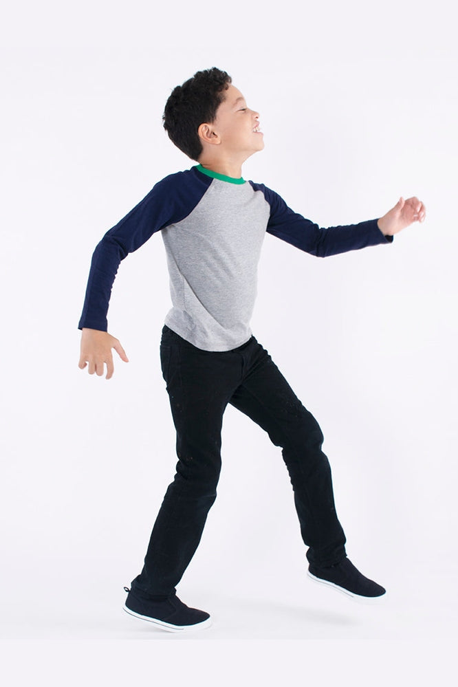 a boy walking wearing a gray and navy blue long sleeve baseball tee and black pants