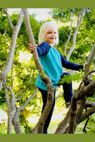 a young child climbing a tree wearing a navy and teal long sleeve baseball tee