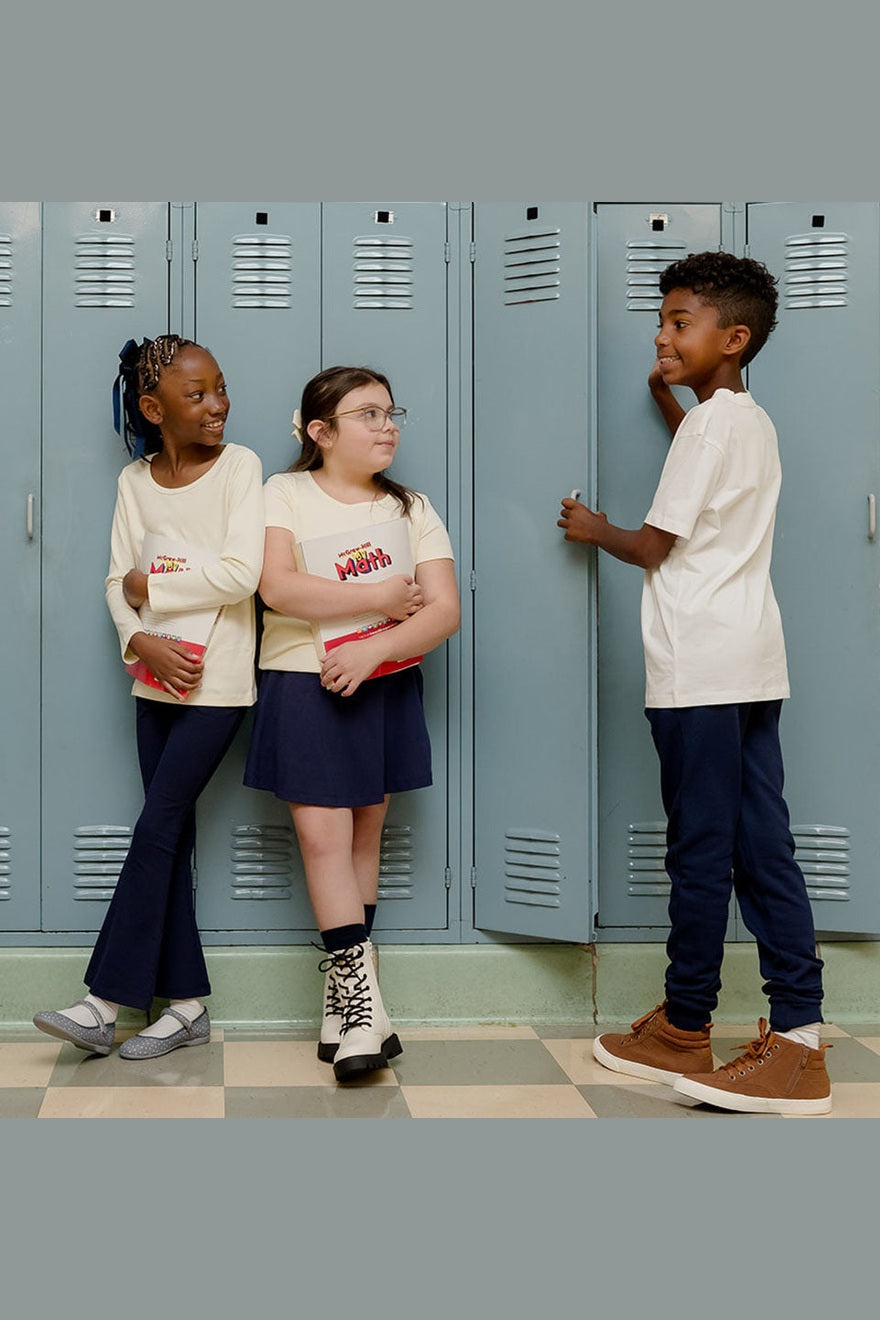 three kids standing against school lockers all are wearing navy blue bottoms and white tops 