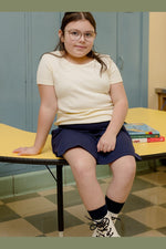girl sitting on a desk wearing an ivory tee shirt and navy skirt 